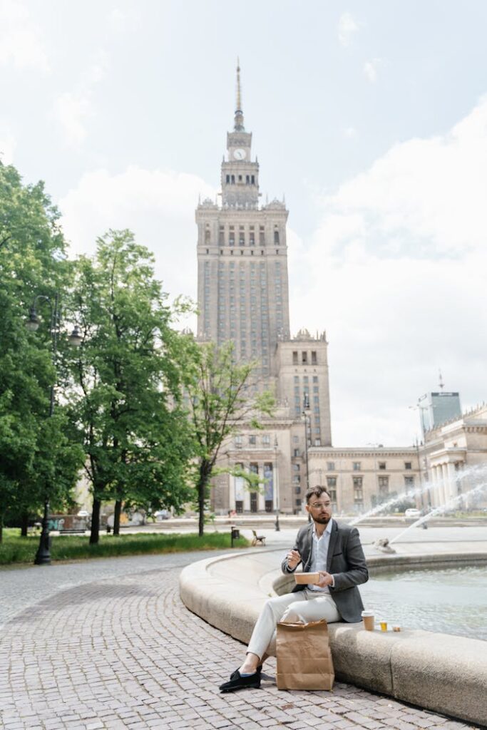 Man in Gray Blazer Eating Beside a Water Fountain