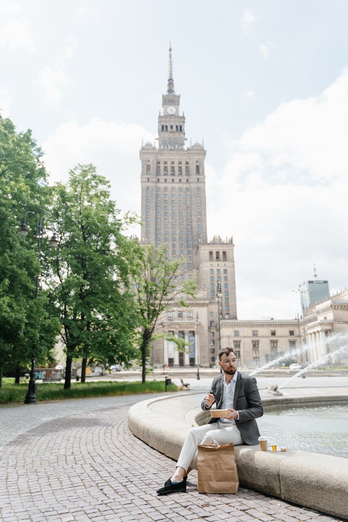 Man in Gray Blazer Eating Beside a Water Fountain